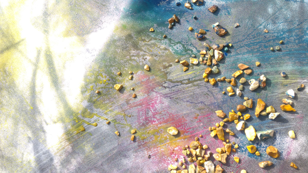 Tinted with stones and sunlight: painted photograph from Residuals #1 drying outside Beckley Village hall, Friday 22 March 2024. Stones prevent wind moving paper while also adding a feature to the installation and photograph.