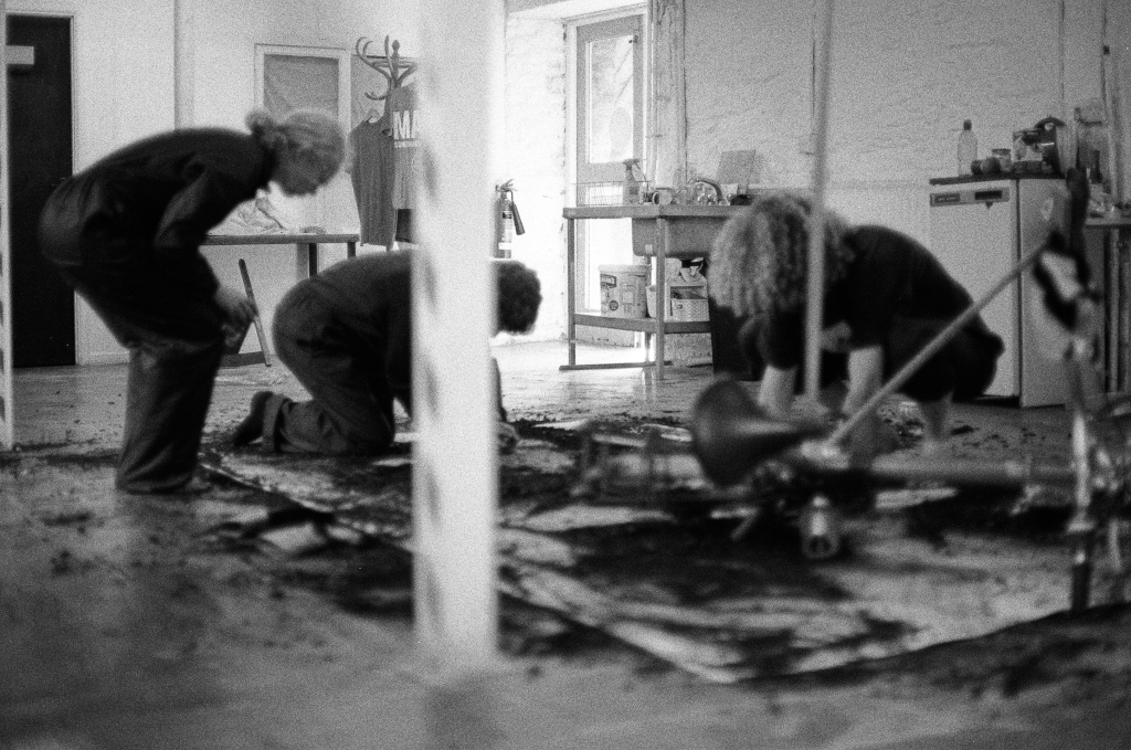 Drawing Residuals #2. Artists Steph, John and Thom working on paper surface with bicycle. Shippon Artists Studios, Dartington Estate, Devon, England. Photo: Andrew Wood