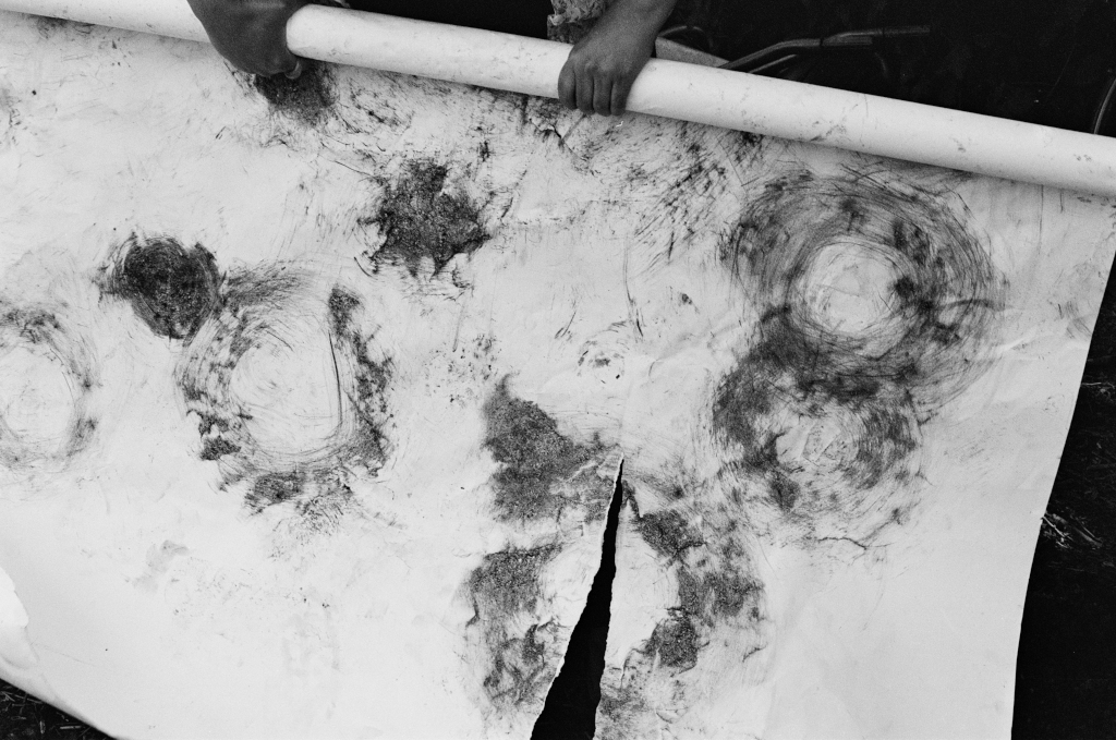 Residuals #4, Debra rolls up the charcoal drawing from the planting performance, Community Garden at Schumacher College, Dartington on Sunday 2 June 2024.