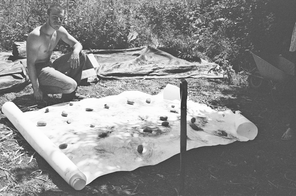 Residuals #4. Jacapo beside the charcoal drawing with potatoes on it, showing their planting positions with the bio-char (charcoal!), Community Garden at Schumacher College, Dartington on Sunday 2 June 2024.